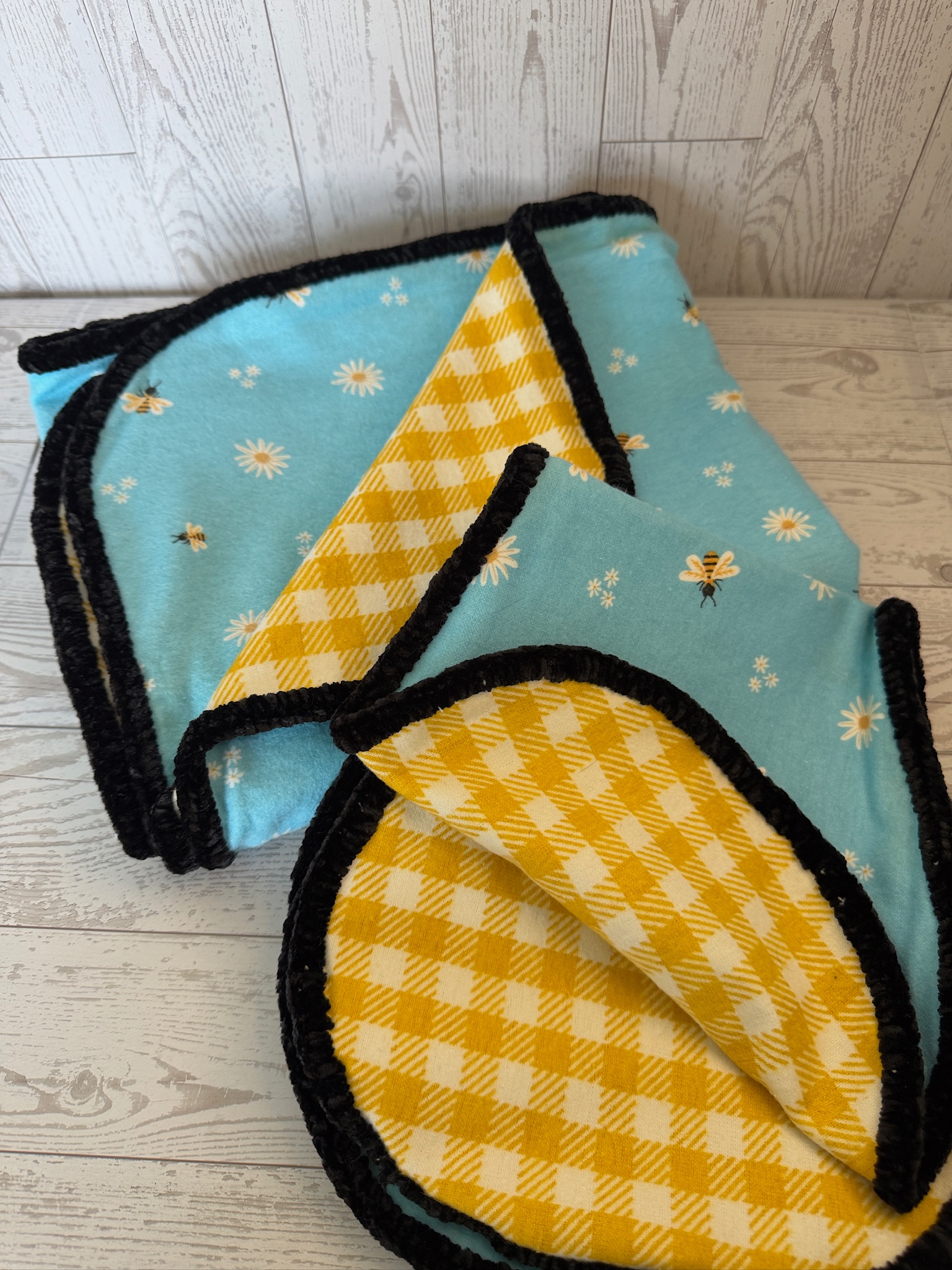 Handmade bee and daisy print aqua flannel baby blanket with yellow gingham reverse and black chenille trim