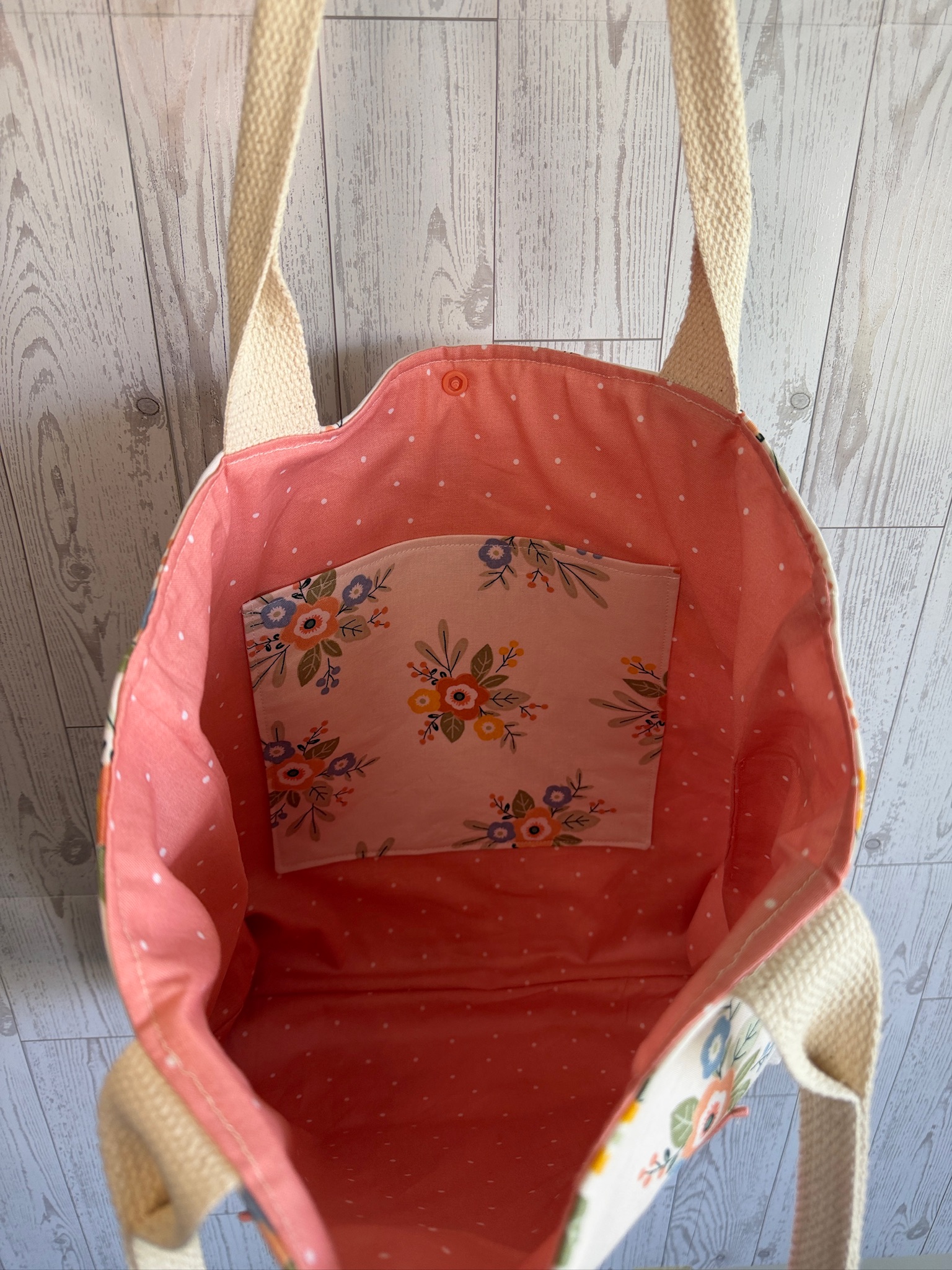 Interior of the cream floral tote bag showing coral lining and a floral slip pocket