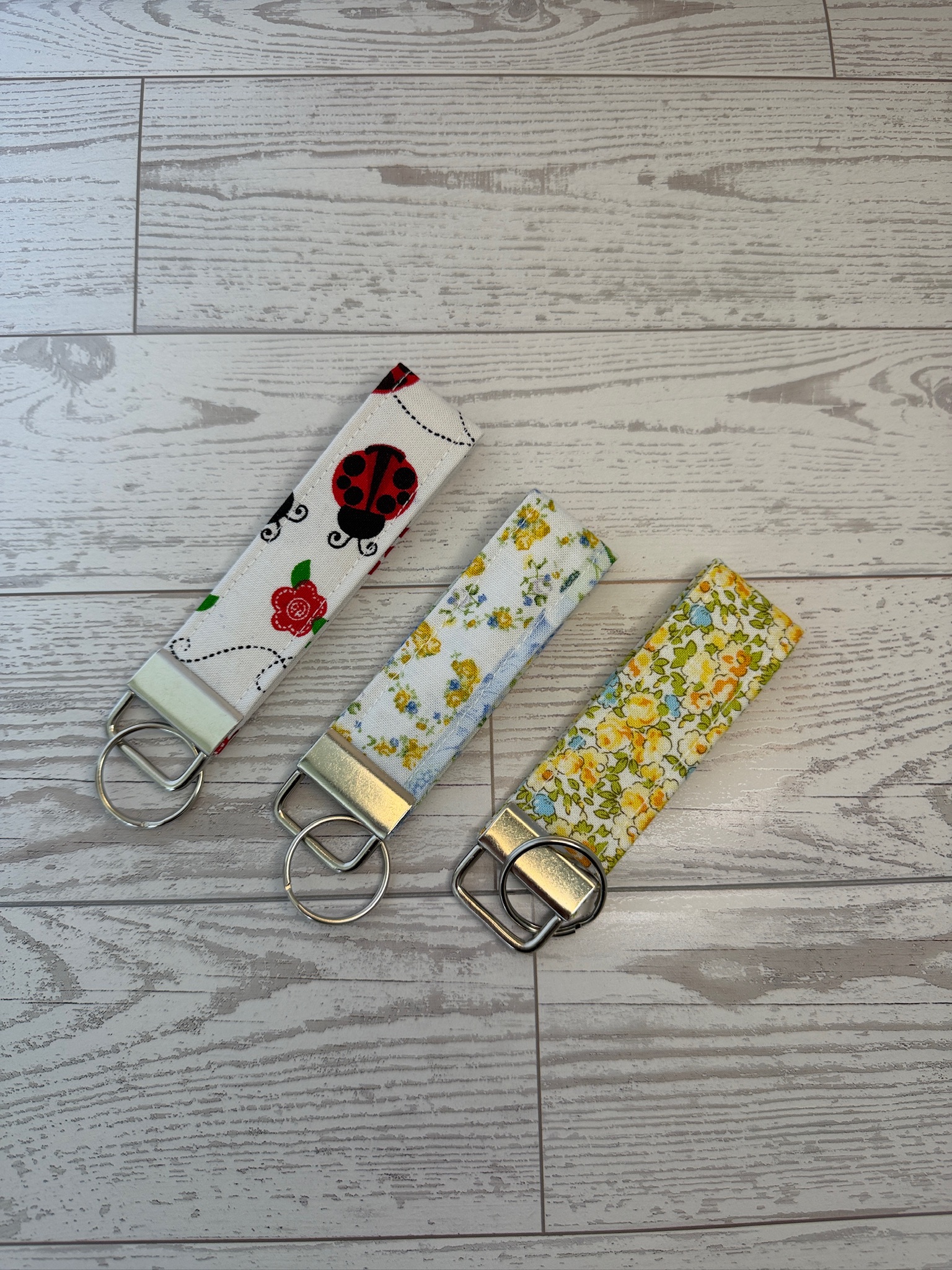 Three handmade key fob wristlets in ladybug, blue floral and yellow buttercup prints on cream fabric