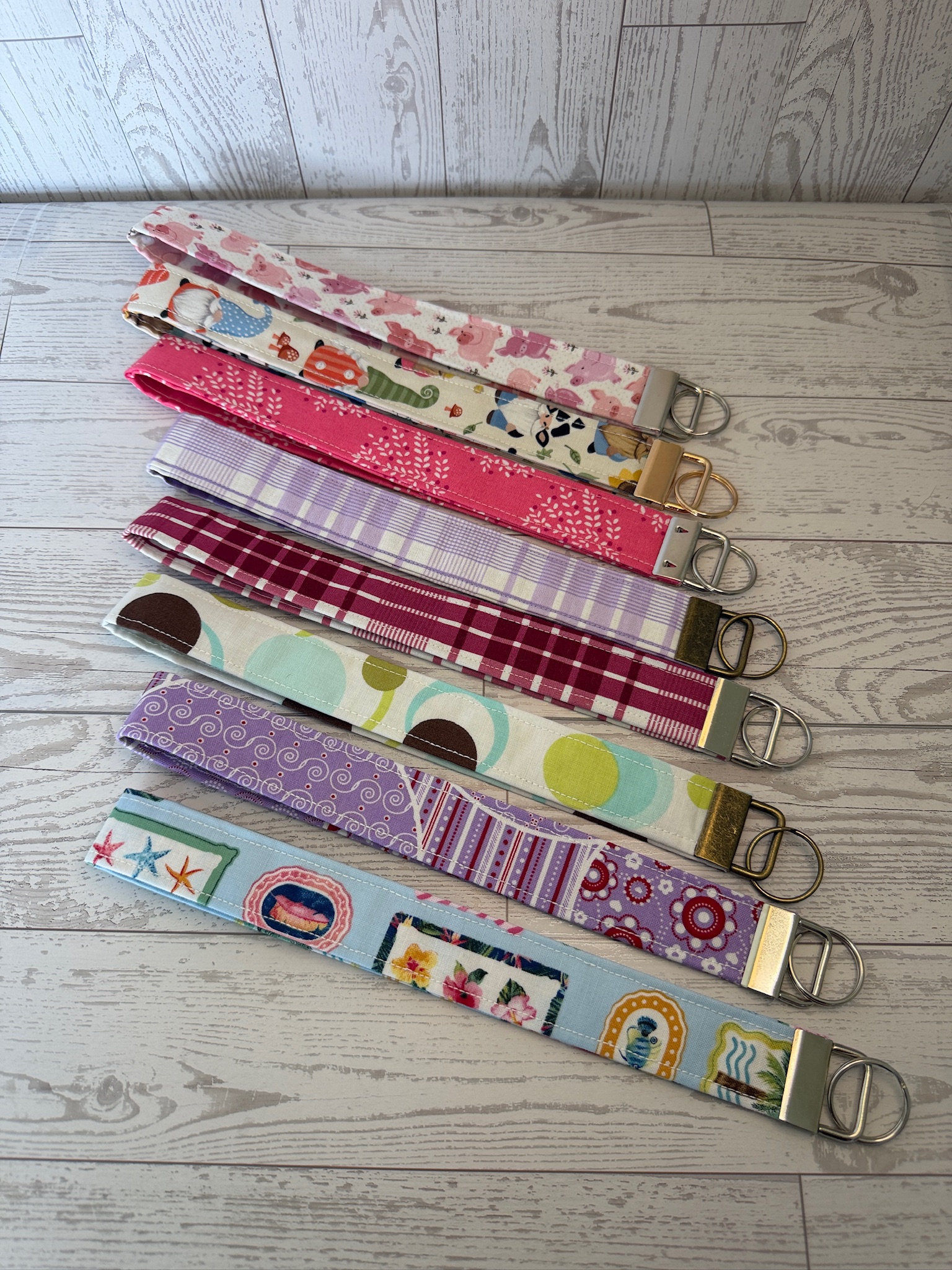 Stack of handmade fabric key fob wristlets in pink floral, plaid and polka dot prints with metal key rings