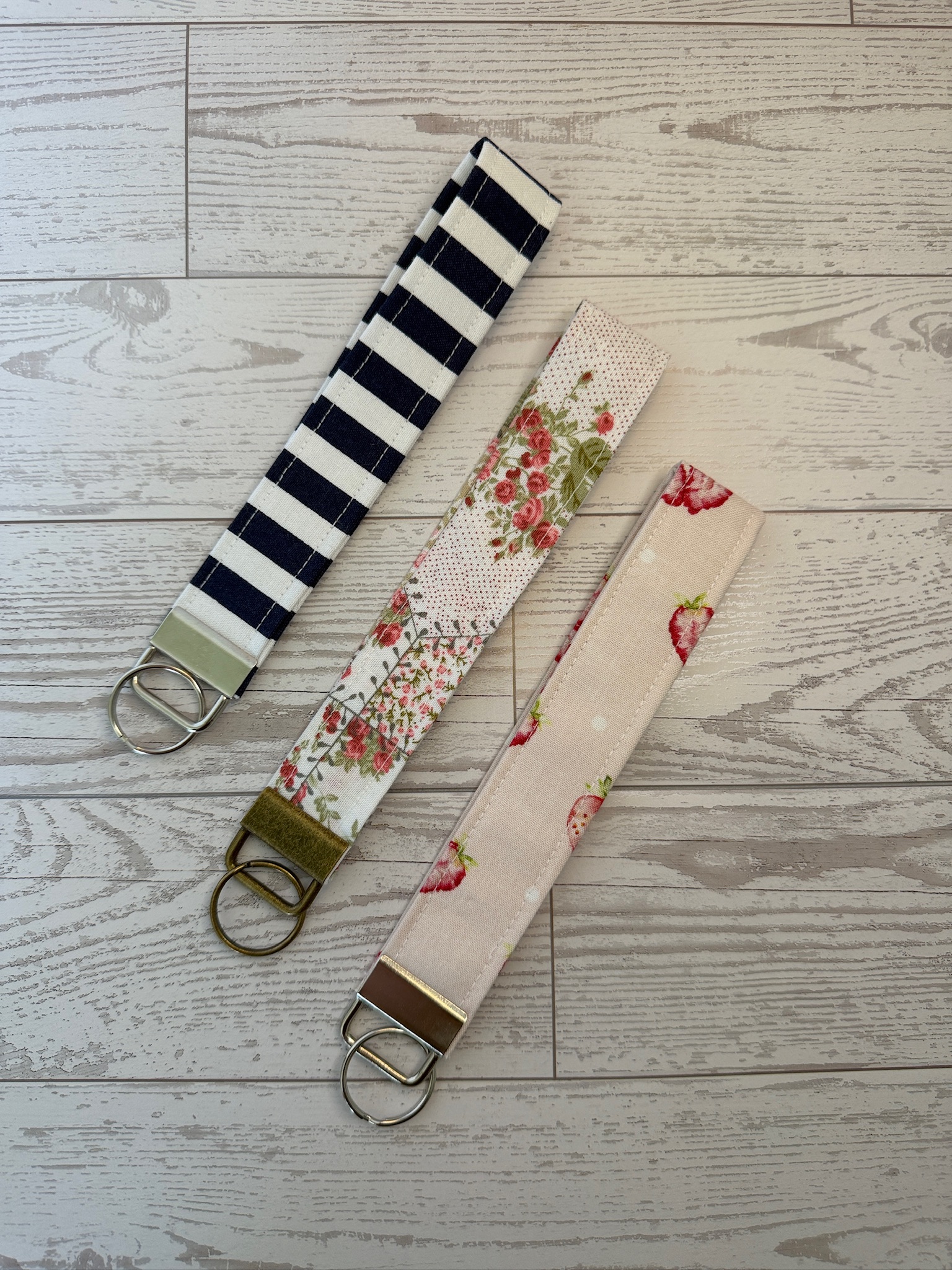 Three handmade key fob wristlets in navy stripe, rose floral and blush strawberry prints