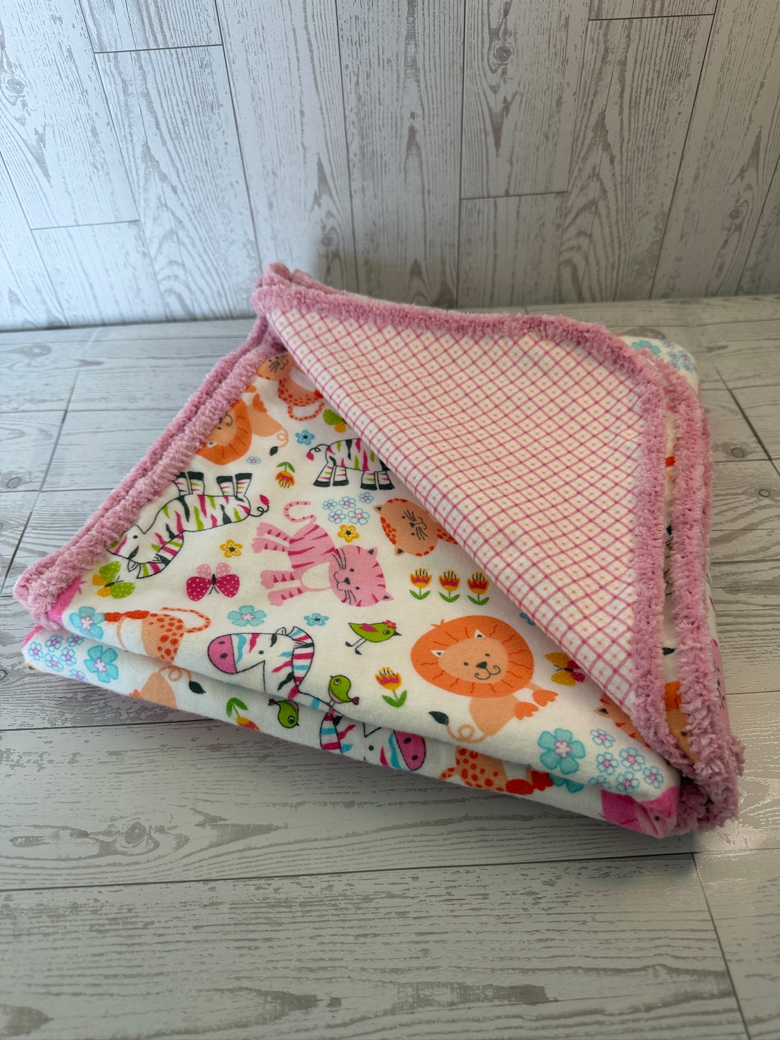 Handmade jungle animal flannel baby receiving blanket folded to show the pink diamond print reverse and chenille trim