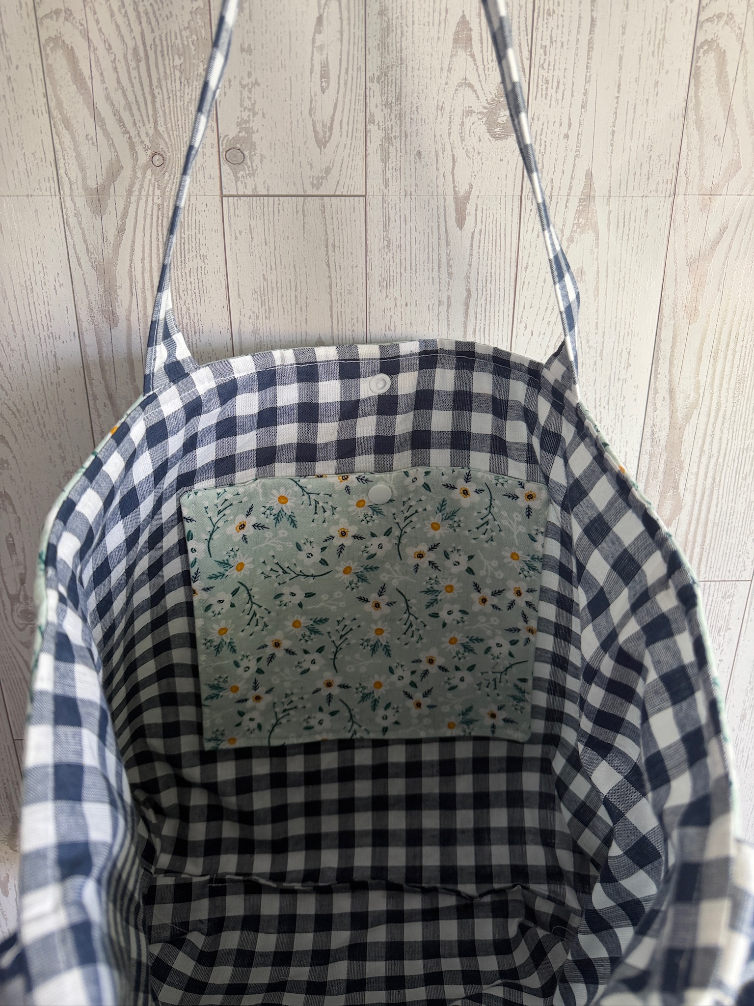 Interior of the blue floral tote bag showing navy gingham lining and a floral slip pocket