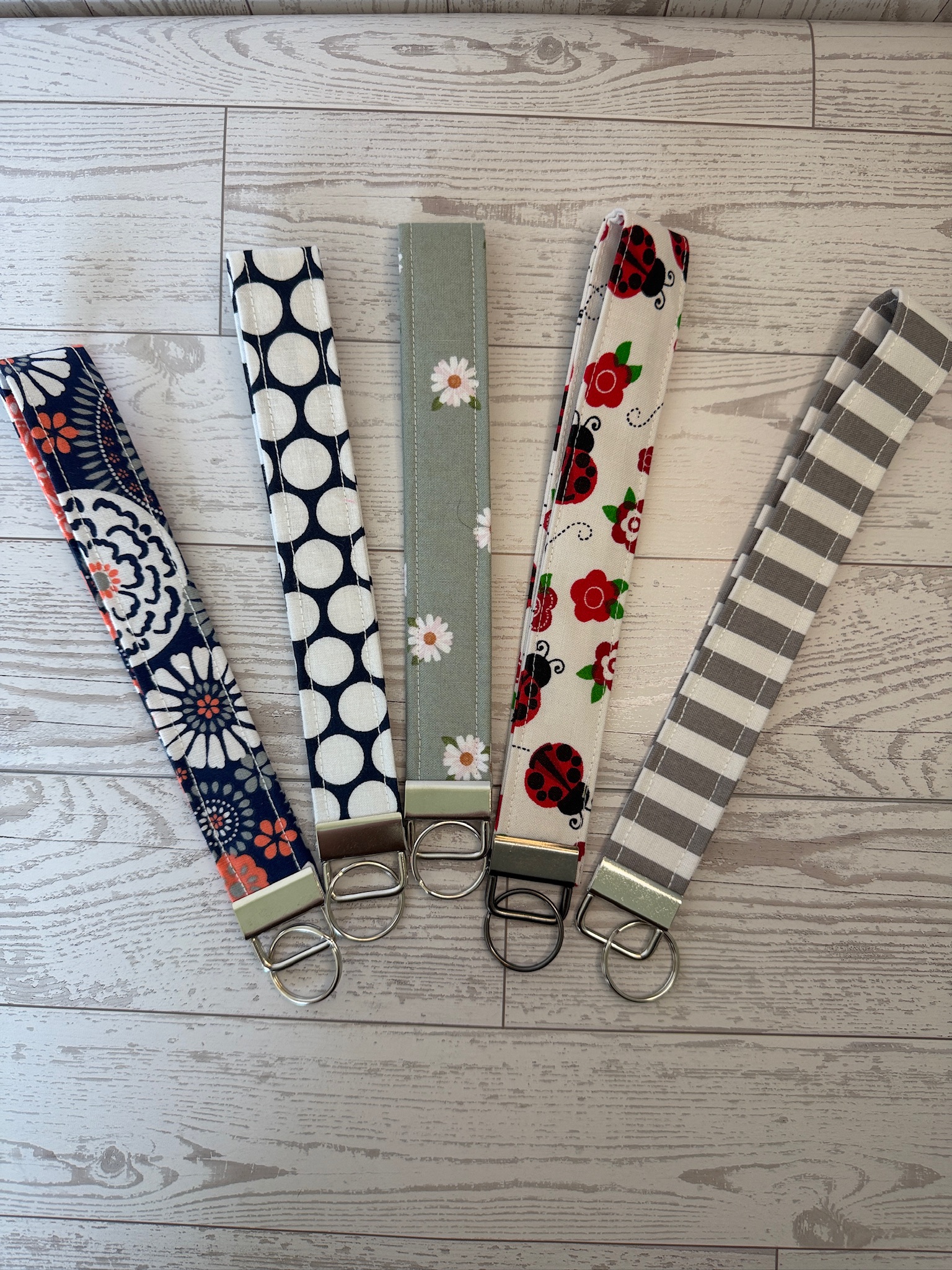 Five handmade key fob wristlets in navy medallion, navy dot, sage daisy, ladybug floral and grey stripe prints