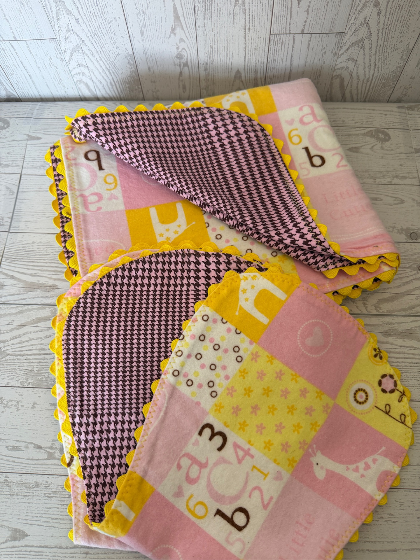 Folded alphabet flannel baby blanket showing the pink houndstooth reverse and scalloped ric-rac trim