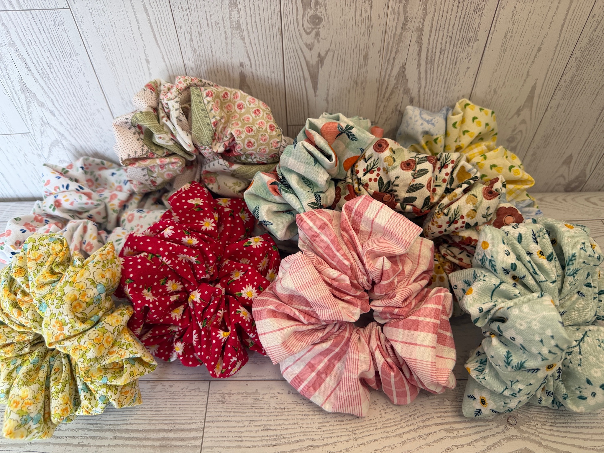 Pile of oversized handmade scrunchies in strawberry, pink plaid and mint floral prints